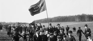 Svartvitt fotografi som visar barn och vuxna som demonstrerar för allmän rösträtt på ett fält, 1901.