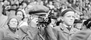 Ett barn håller en kamera framför ansiktet och fotograferar