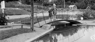 Bilden föreställer två barn som står på en liten bro över en plaskdam i en park 1940.