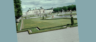 Ett stort slott i en grönskande park och mot blå himmel.