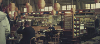 Människor sitter vid små bord och äter på restaurang med träinredning