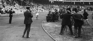 Målgång i 10 000 meter gång. En fotograf står vid mållinjen och en vitklädd löpare är på väg fram på banan inne på Stockholms stadion