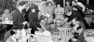 Män och kvinnor står och sitter runt ett bord med händerna för arbete