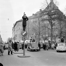 Narvavägen. Folksamling tittar på studentkarneval. Folk har klättrat upp i träd, på biltak och i gatlyktor för att kunna se