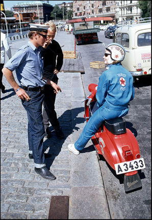 Person på vespa pratar med två unga män.