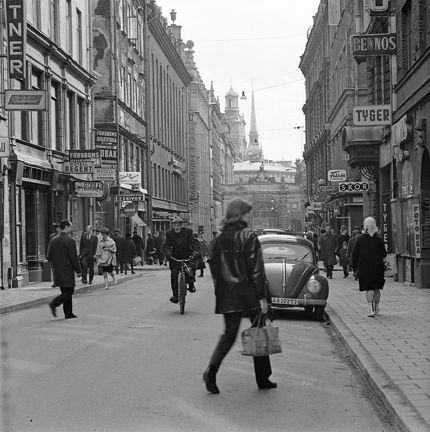 Människor rör sig längs gatan. Butiksskyltar.