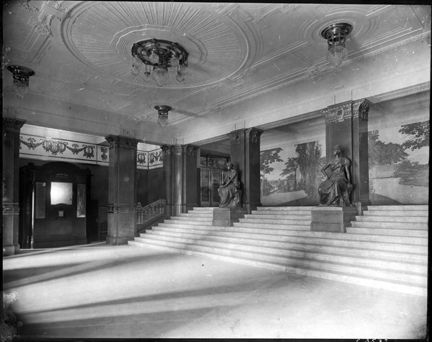 Entréhall med trappa, skultpturer och väggmålning.