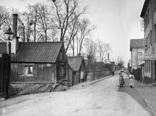 Två flickor passerar Åsögatan 141 österut från Skeppargränd. Nuv. Åsögatan 195. T.h. kv. Oljan