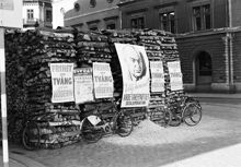 Vedstapel med valaffischer från Arbetarepartiet socialdemokraterna och Högern, samt en affisch från Gröna Lund