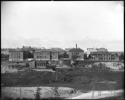 Ett stort antal byggnader i tegel ligger på rad på en kulle. Framför husen är det öppen mark.