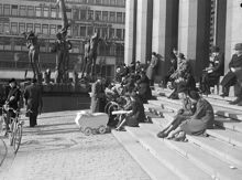 Hötorget 8. Folk sitter på trappan till Konserthuset i vårsolen