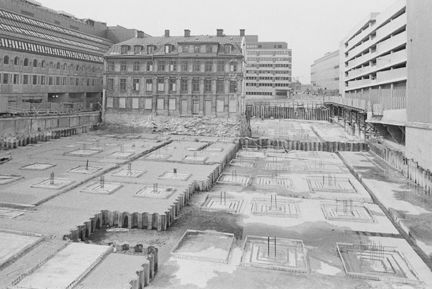 En stor obebyggd yta, där plattgjutning pågår. Omgivande äldre och modernare fasader.