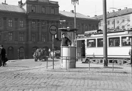 En polis dirigerar trafik i en cylinderformad kur mitt i bilden. Till höger syns en spårvagn och i bakgrunden en palatsliknande fasad