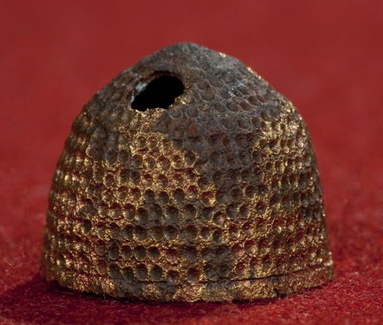 Medeltida fingerborg av förgylld koppar. Fotograferad mot röd bakgrund. 