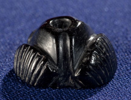 Svart medeltida radbandspärla av jet (gagat). Fotograferad mot blå bakgrund. 