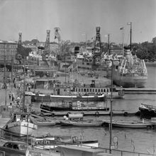 Skeppsbron. Fyra lyftkranar lossar gods från Finlandsbåtarna till järnvägsvagnar uppställda framför tullhusen
