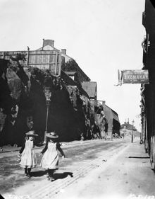 Två flickor befinner sig vid hörnet av Renstiernas Gata och Åsögatan österut. Berget ska sprängas bort för breddning av Renstiernas Gata och Åsögatan. Husen på höjden ligger vid Beckbrännargränd