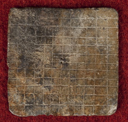 Medeltida spelbricka av bly med 12 x 12 rutor inristade. 
