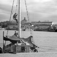 Segelbåt vid Strandvägskajen. Skeppsholmen med krigsfartyg i bakgrunden
