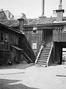 Gårdssidan vid Styrmansgatan 14. Elkablar fästa i väggen hänger över gården. I trappan står en krukväxt