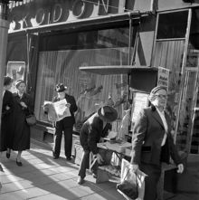 Drottninggatan 65. Tidningsförsäljning utanför Kembels skor