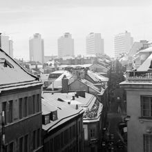 Vy över taken längs Jakobsbergsgatan västerut från Birger Jarlsgatan till Malmskillnadsgatan. Höghusen i kv. Beridarbanan i fonden