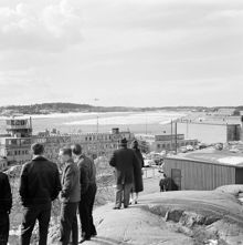 Utsikt från Ranhammarshöjden över Bromma flygplats, med byggnader och trafikledartorn. Grupp av åskådare i förgrunden, i bakgrunden flygplan i luften