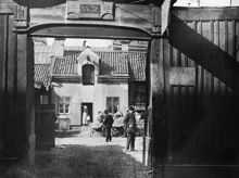 Stora Badstugatan 31. Vy genom porten i planket mot gården som på andra sidan vetter mot Lilla Badstugatan 4. Några hästar med vagnar står på gården