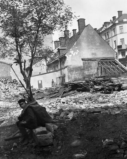 En pojke med en säck på ryggen sitter på gårdssidan vid rivna Skeppargatan 35. Huset vid Linnégatan 50 i fonden. Nuvarande Skeppargatan 43 - Linnégatan 48-50