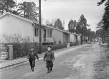 Västberga, Korpmossen. Två barn promenerar i småstugeområde. I bakgrunden LM Erikssons torn