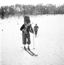 Stockholmarna vintersportar. En man åker skidor med ett barn på axlarna
