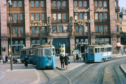 Blåvita spårvagnar, promenerande människor och husfasad i bakgrunden