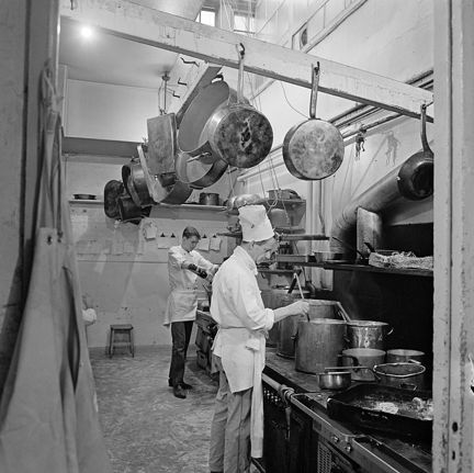 En yngre och en &#xE4;ldre man r&#xF6;r i en rad grytor p&#xE5; en spis. K&#xF6;ksredskap h&#xE4;nger i taket.