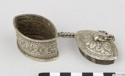 Liten kalkdosa i silver & koppar. Öppen. Dosan är bara 5cm lång, med kedjat lock, och blommönster på utsidan. Den kommer från Indien. Dosan har använts till släckt kalk, ett puder som man behöver om man tuggar betel. Beteltuggning ger milt rus och röda tänder. Det har varit vanligt i Sydostasien. 