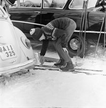 Pojke spänner fast sina skidor, vid en bilparkering