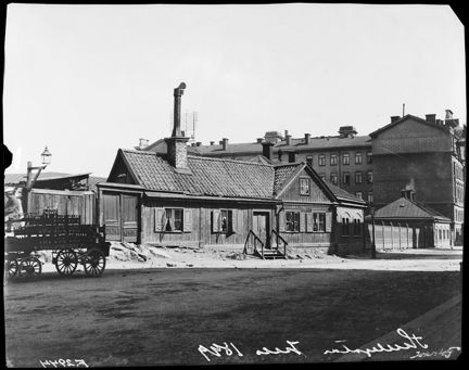 Framför ett gammalt trähus med hög skrosten står en vagn lastad med drickabackar.