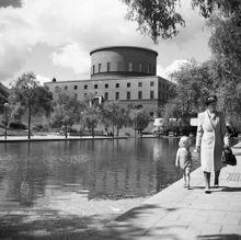 Observatorielunden. Kvinna och barn går hand i hand längst med plaskdamm. Stadsbiblioteket i bakgrunden