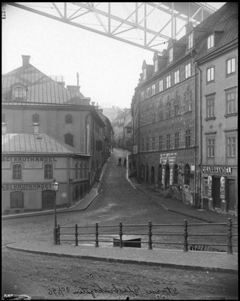 En smal och brant gata leder uppför ett berg. Gatan kantas av lite större stenhus och högt över alltihop går en gångbro av gjutjärn. Platsen ligger öde. Få människor syns. 