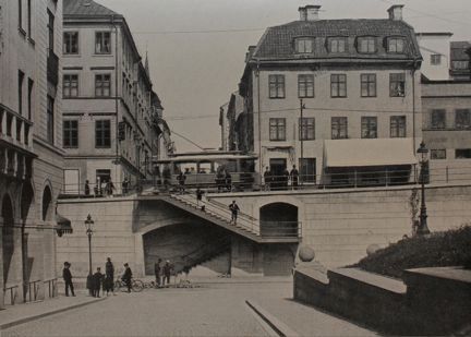 Byggnader, gator mellan vägar i olika plan, en spårvagn och människor till fots och på cykel.
