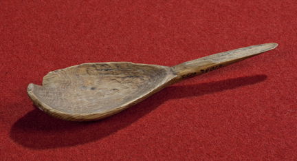 Medeltida träsked med droppformat skedblad. Fotograferad mot röd bakgrund. 