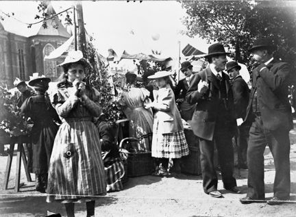 Marknadsbesökare på Lövmarknaden vid Riddarholmskanalen på Riddarholmen. Flickan i förgrunden blåser i en lergök och i bakgrunden skymtar Riddarholmskyrkan.