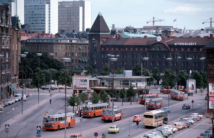 I mitten ett runt hus i två våningar. Framförhuset röda bussar och i bakgrunden större hus och Hötorgsskraporna.