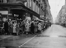 Hörnet Drottninggatan och Klarabergsgatan. Gustaf VI Adolf fyller 70 år och åker i kortege genom staden. Längs kortegens väg stod stockholmare och väntade. T.h. vy Drottninggatan norrut