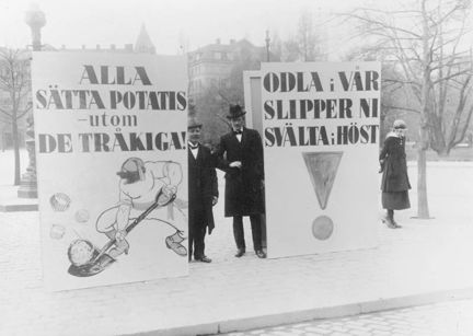 några män står vid stora skyltar där det står "alla sätta potatis utom de tråkiga" och odla i vår slipper ni svälta i höst"