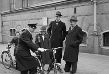 Sofia folkskola har trafikundervisning. Konstapel Sven Ek undersöker femteklassaren Monica Landgrens cykel medan överståthållare Hagander och överlärare R. Agvald ser på