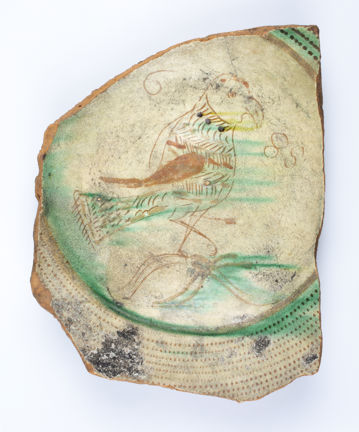 Framsida av fat. Fatet är blyglaserat och har handmålad dekor i form en fågel.