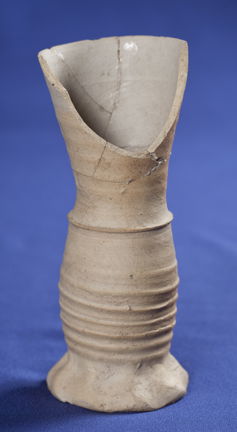 Medeltida dryckesbägare av Siegburgtyp av gråvit lera. Fotograferad mot blå bakgrund.