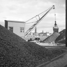 Kajen vid Söder Mälarstrand. En kran i arbete vid grushögar. Riddarholmen i fonden
