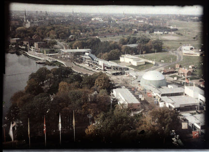 En flygbild tagen över ett större fält, Gärdet i Stockholm. Längs en kanal syns ett utställningsområde med en mängd vita, funktionalistiska byggnader. Intill utställningsområdet syns ett stort grönt fält och i fonden syns stadsbebyggelsen i innerstaden.