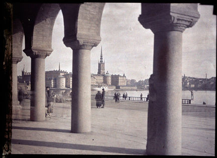 Bakom arkadens pelare syns människor flanera. Riddarholmen i bakgrunden.